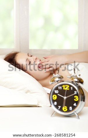 Sleeping woman resting in bed with alarm clock ready to wake her in the morning