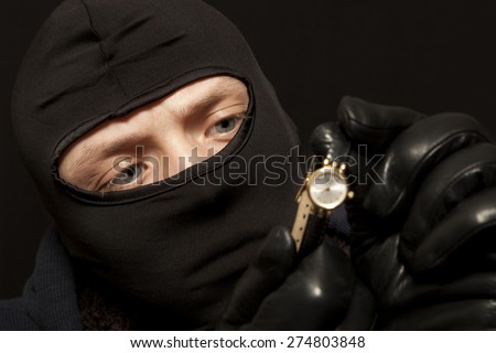 Thief. Man in black mask with a golden watch. Focus on thief