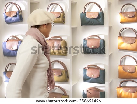 Shopping woman chooses lady's handbag in store. Woman looking to lady's handbag or shop window.