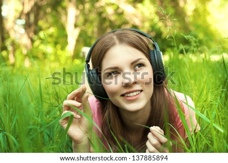 Close up portrait of Pretty young girl listening music lying at the grass