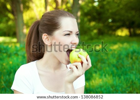 Close up portrait of girl bites an apple outdoor
