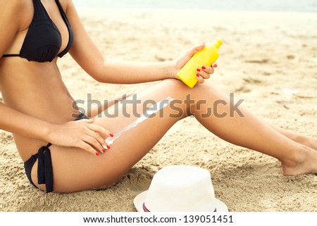 woman moisturizing applying sun cream on her tanned body and legs legs