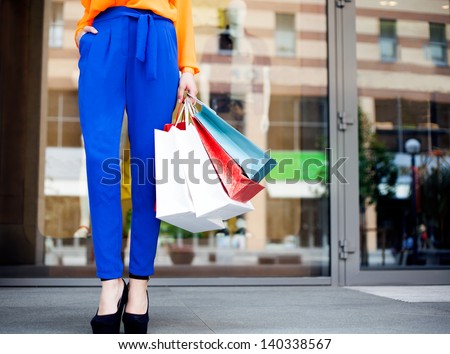Girl holding shopping bags in one hand, legs in blue trousers