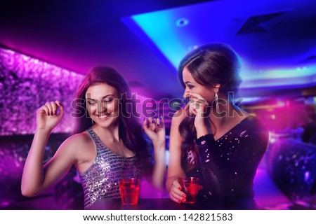 Two Happy Girl Friends At The Club, Laughing And Drinking