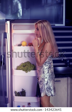 Woman wearing pajamas looking in fridge at night kitchen
