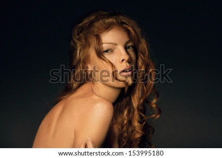Fashion portrait of red-haired freckled young woman with beautiful long wavy hair over dark background