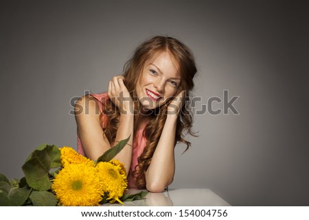 Beautiful red-haired young woman with yellow flowers, smile , horizontal close up portrait, gray background