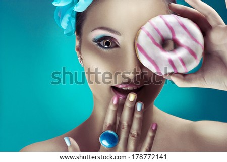 Beauty portrait of girl holding a donut with pink icing, looking through hole