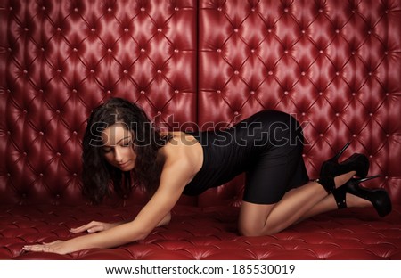 sexy women in short black dress lying on red leather sofa wall, looking down