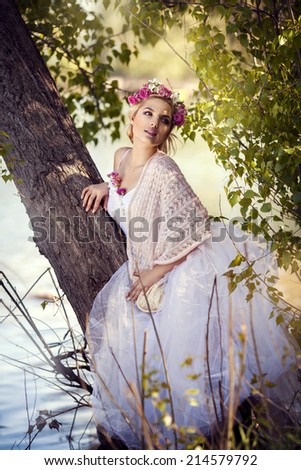 Young beautiful woman in white dress in blooming garden with roses on her head