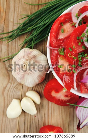 healthy appetizer : fresh tomato salad in white bowl with bunch of chives and raw tomatoes on twig , violet onion, garlic over wooden table