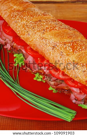 french sandwich on red plate : baguette with smoked sausage over wooden table