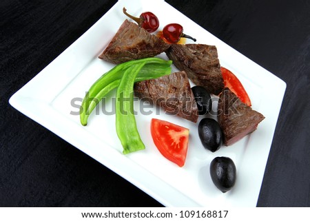 meat food : roast beef fillet mignon served on white plate with apples dill and tomatoes over black wooden table