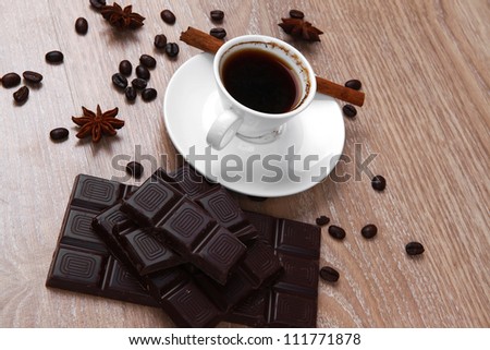 sweet hot drink : black Turkish coffee in small white mug with coffee beans spilled over a wooden table with stripes of dark chocolate and cinnamon stick
