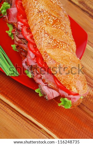 french sandwich : fresh white baguette with chicken smoked sausage on red ceramic plate over wooden table