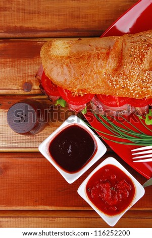 business lunch french sandwich on red plate : baguette with smoked sausage over wooden table