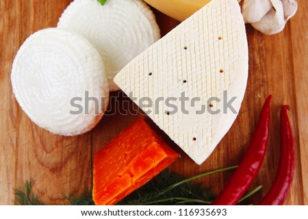 several soft and hard types of french cheese on wooden board with hot peppers and dill isolated on white background