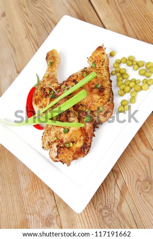 meat food : chicken legs garnished with green peas and hot chili peppers on white plates over wooden table