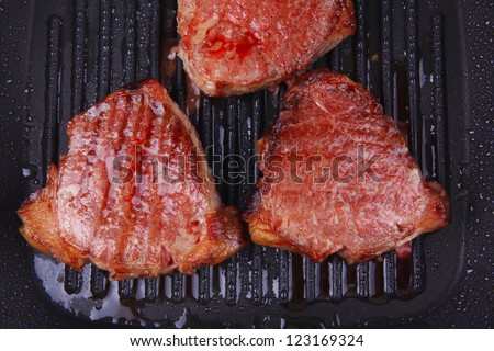 fresh grilled bloody beef steaks on black grill plate isolated on white background