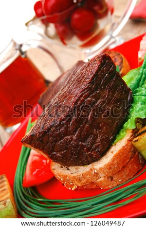 savory food : roast beef garnished with vegetables , juice and olives on red plate over wooden table