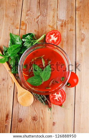 cold fresh diet tomato soup with basil thyme and raw tomatoes in transparent bowl over red mat on wood table ready to eat