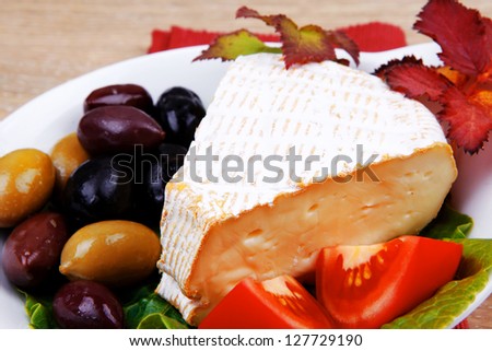 aged brie cheese on salad in white dish over red cloth on with olives and tomato over wooden table