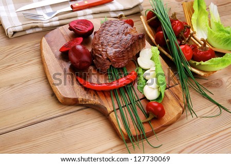 meat food : roast beef garnished with green staff and red chili hot pepper on wooden table with cutlery