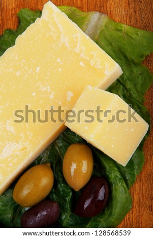 yellow edam cheese on wooden platter with olives and tomato isolated over white background