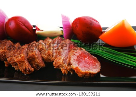 main course : roast red meat slices served on black plate with vegetables on spit isolated on white background
