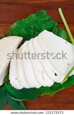 mediterranean cuisine : raw soft feta white cheese round with slices on wooden plate isolated over white background