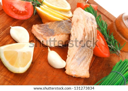 savory sea fish entree : roasted salmon fillet with green onion, red cherry tomatoes pieces, glass pepper grinder, rosemary twigs and lemon on wooden board isolated on white background