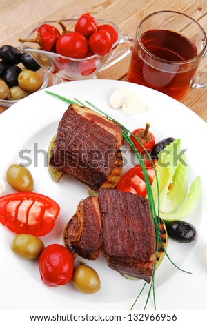 grilled meat : beef ( lamb ) garnished with tomatoes , green and black olives, tomatoes and juice on wooden table
