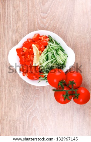 whole tomatoes on branch with salad of shredded tomatoes and cucumbers on white dish over wood table