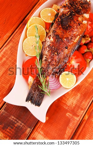 main course: whole fried sunfish on wooden table with lemons and peppers