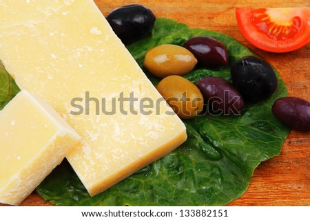 solid parmesan on wooden platter with olives and tomato isolated over white background
