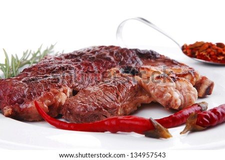 meat food : grilled beef steak on white plate with red thin pepper , spices and rosemary isolated over white background