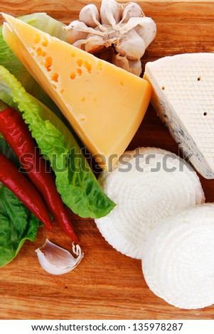 several  delicatessen types of cheese on wooden board with hot peppers and dill isolated on white background