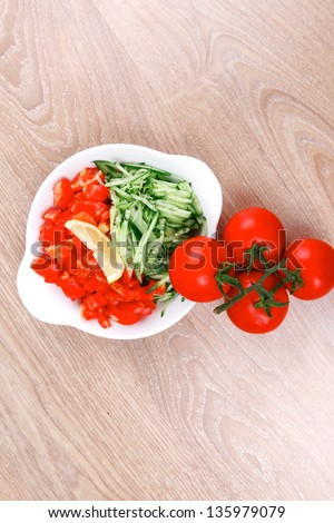 whole tomatoes on branch with salad of shredded tomatoes and cucumbers on white dish over wood table
