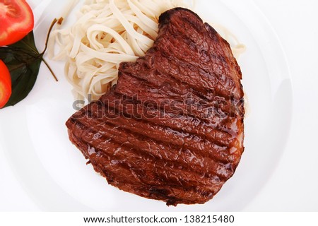 italian cuisine : grilled beef steak with pasta and tomatoes on basil leaf on plate isolated over white background