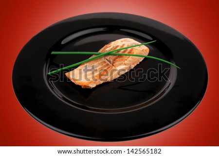 savory sea fish entree : roasted salmon fillet with green onion, on black dish isolated over white background