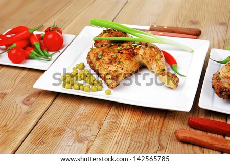 meat food : chicken legs garnished with green peas and and cutlery on white plates over wooden table