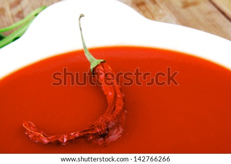 diet food : hot tomato vegetable soup with basil thyme and raw tomatoes in white round bowl over red mat on wood table ready to eat