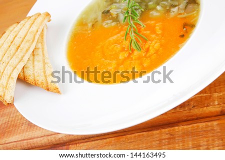 european cuisine: vegetable soup served with toasts on white dish on wooden table