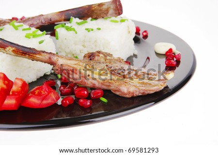 main course: grilled ribs with rice and tomatoes on black dish over white background . shallow dof