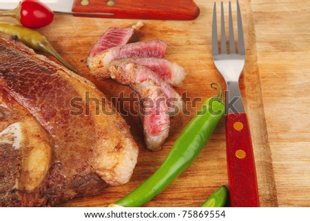 fresh roasted beef meat steak sliced on wooden board with red hot pepper cutlery isolated  over white background