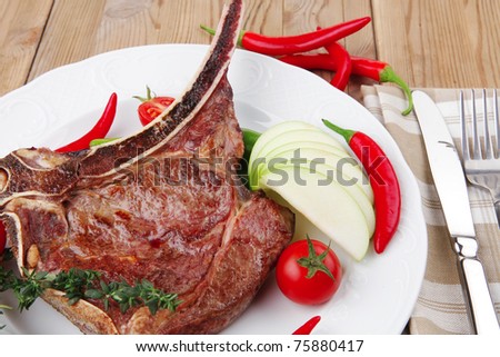 meat food : grilled beef spare rib on white dish with thyme pepper and tomato on wooden table
