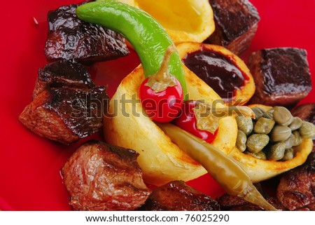 european food: roast beef meat over red plate isolated on white background with hot peppers, capers , olives oil , and bbq sauce