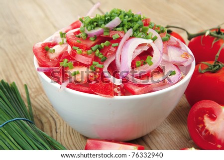 healthy appetizer : fresh tomato salad in white bowl with bunch of chives and raw tomatoes on twig , violet onion, over wooden table