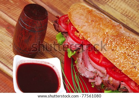 french sandwich : fresh white baguette with chicken smoked sausage on red ceramic plate over wooden table
