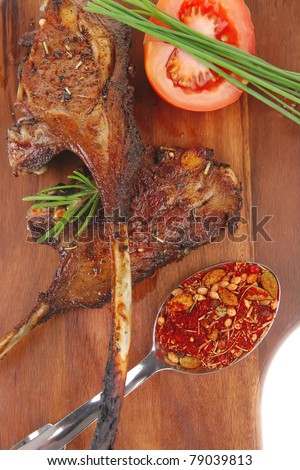 meat on wooden plate : roast ribs on wood with tomatoes chives and dry spices isolated on white background